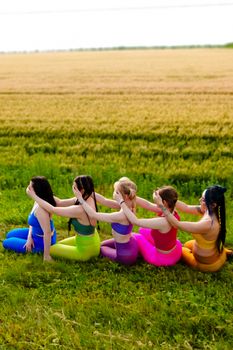 A group of women practicing yoga outdoors wearing colorful outfits in a field.