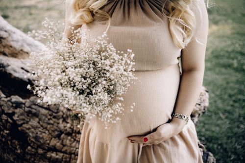 Free Pregnant woman in beige dress holding baby's breath bouquet outdoors. Stock Photo
