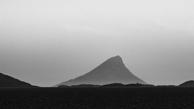 Black and white view of a mountainous landscape in Nordland, Norway, with sea foreground and misty atmosphere.