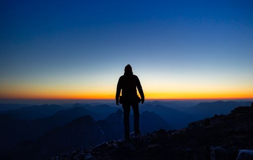Free Silhouette of a hiker observing a breathtaking sunrise over the Austrian Alps. Stock Photo