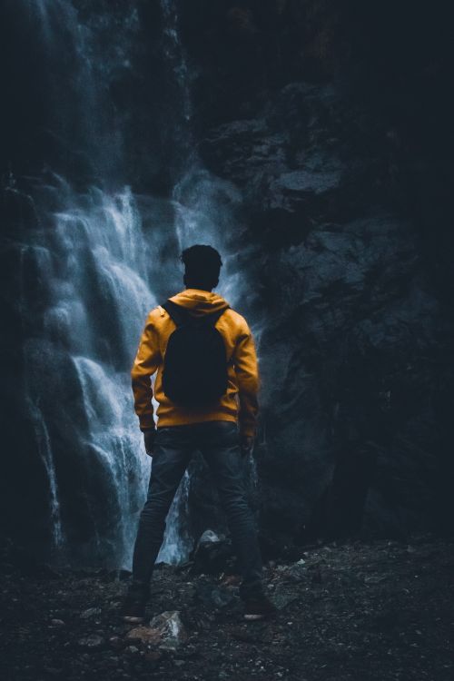 Free Person in a yellow jacket observes a waterfall in Lachung, creating a mysterious adventure vibe. Stock Photo