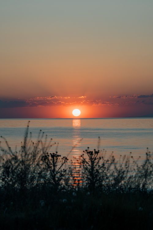 Free A tranquil sunset setting with vibrant skies reflecting over a calm ocean, perfect for peaceful and inspiring themes. Stock Photo