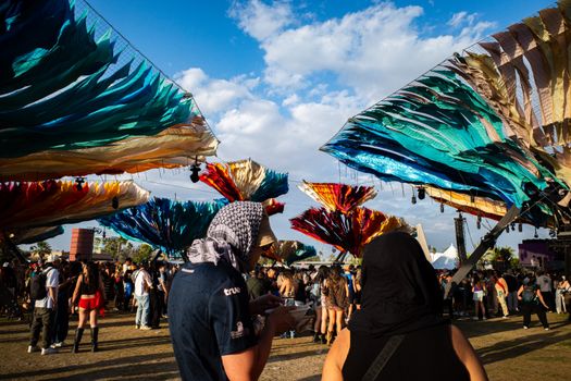 A lively outdoor festival scene with colorful fabric canopies and diverse crowd enjoying the event.
