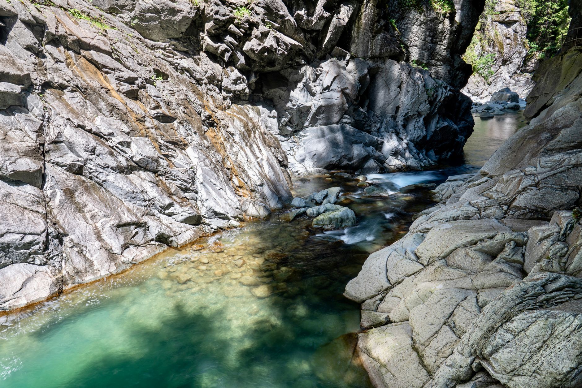 Serene view of a rocky gorge with clear turquoise water flowing through, under daylight.