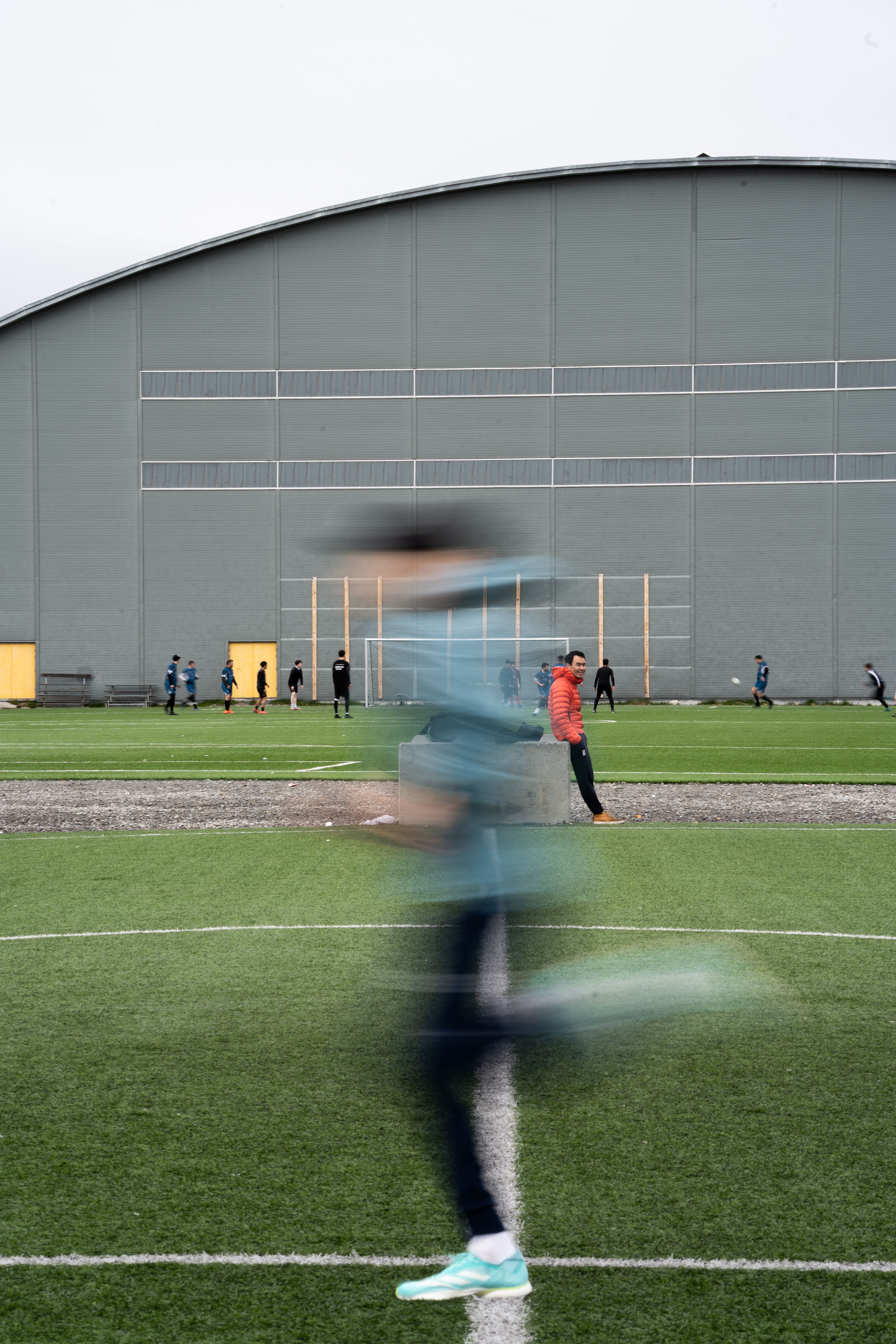 A blurred athlete running on a sports field in front of an indoor sports facility in Nuuk, Greenland.