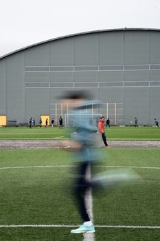 A blurred athlete running on a sports field in front of an indoor sports facility in Nuuk, Greenland.