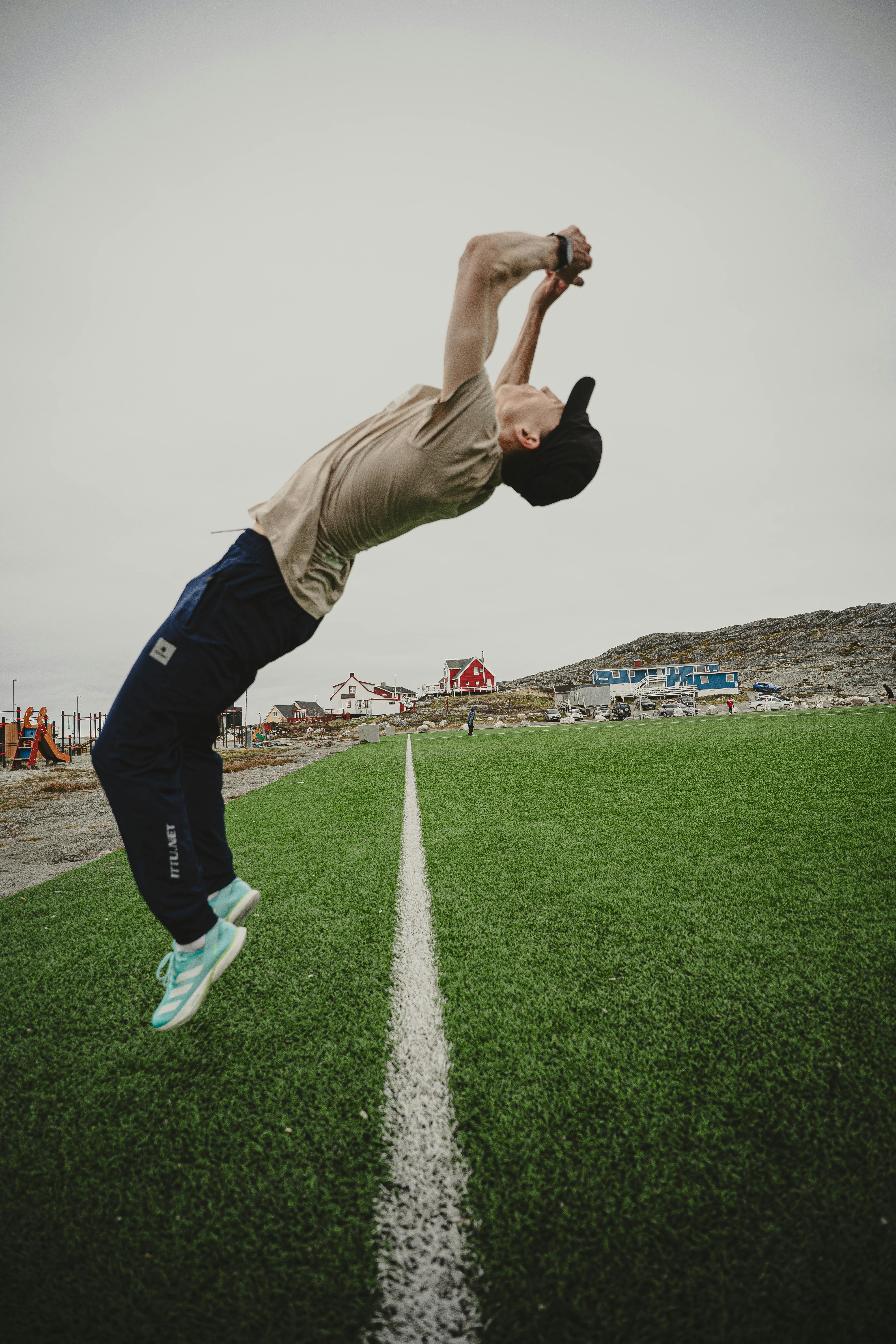 An athletic man performs a backflip on a sports field in Nuuk, Greenland. Showcasing agility and energy.