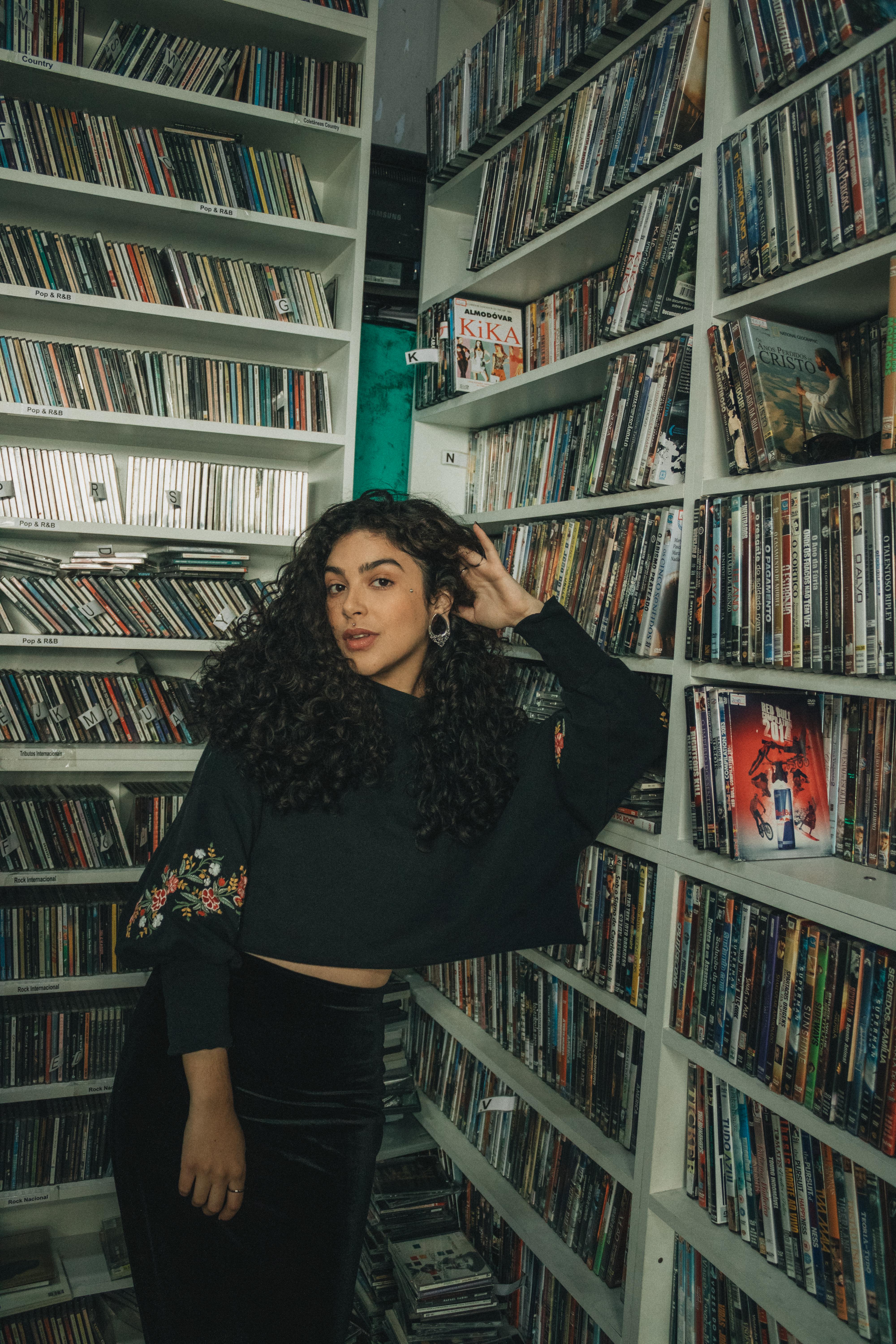 Woman posing in a DVD store, showcasing style amidst shelves of movies. Vibrant and trendy setting.