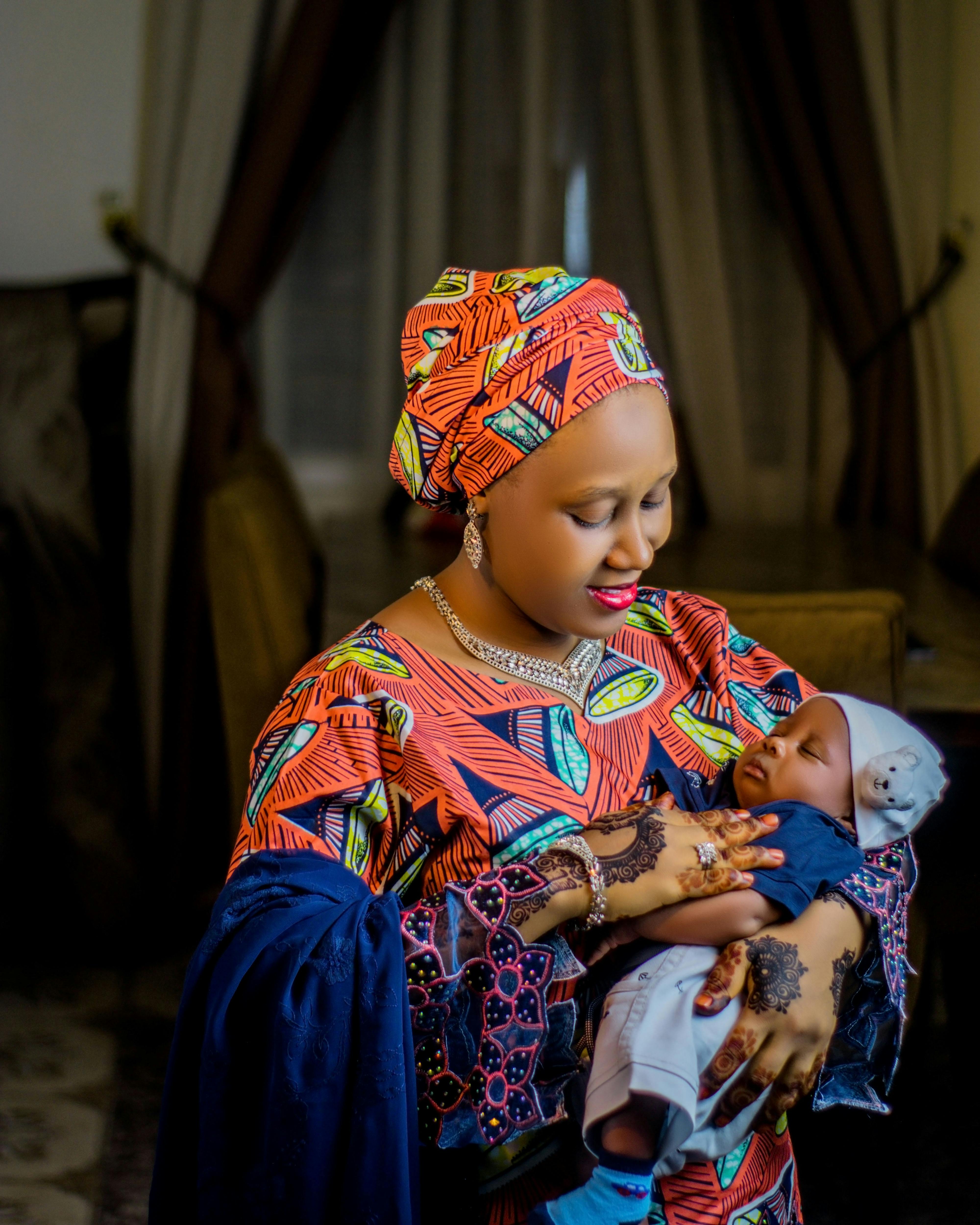 Woman in colorful traditional clothing joyfully holding baby indoors.