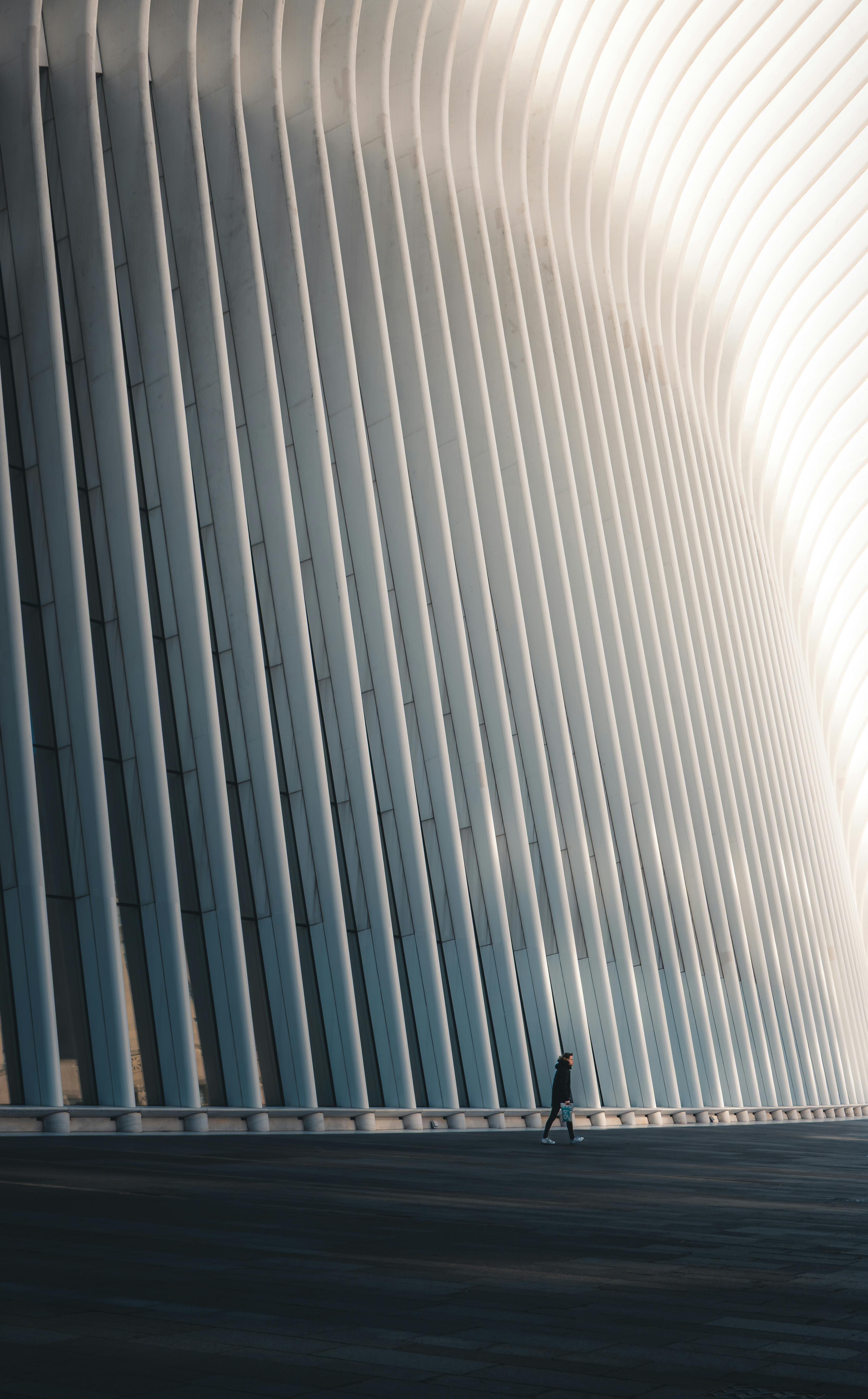 A lone figure walks by an imposing modern architectural facade with striking curves and lines.