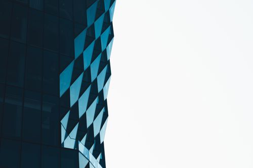 Free Close-up of a building facade featuring a modern geometric design with blue tinted glass. Stock Photo