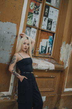 Fashionable woman with tattoos poses confidently against a graffiti-covered wall. Urban vibe.