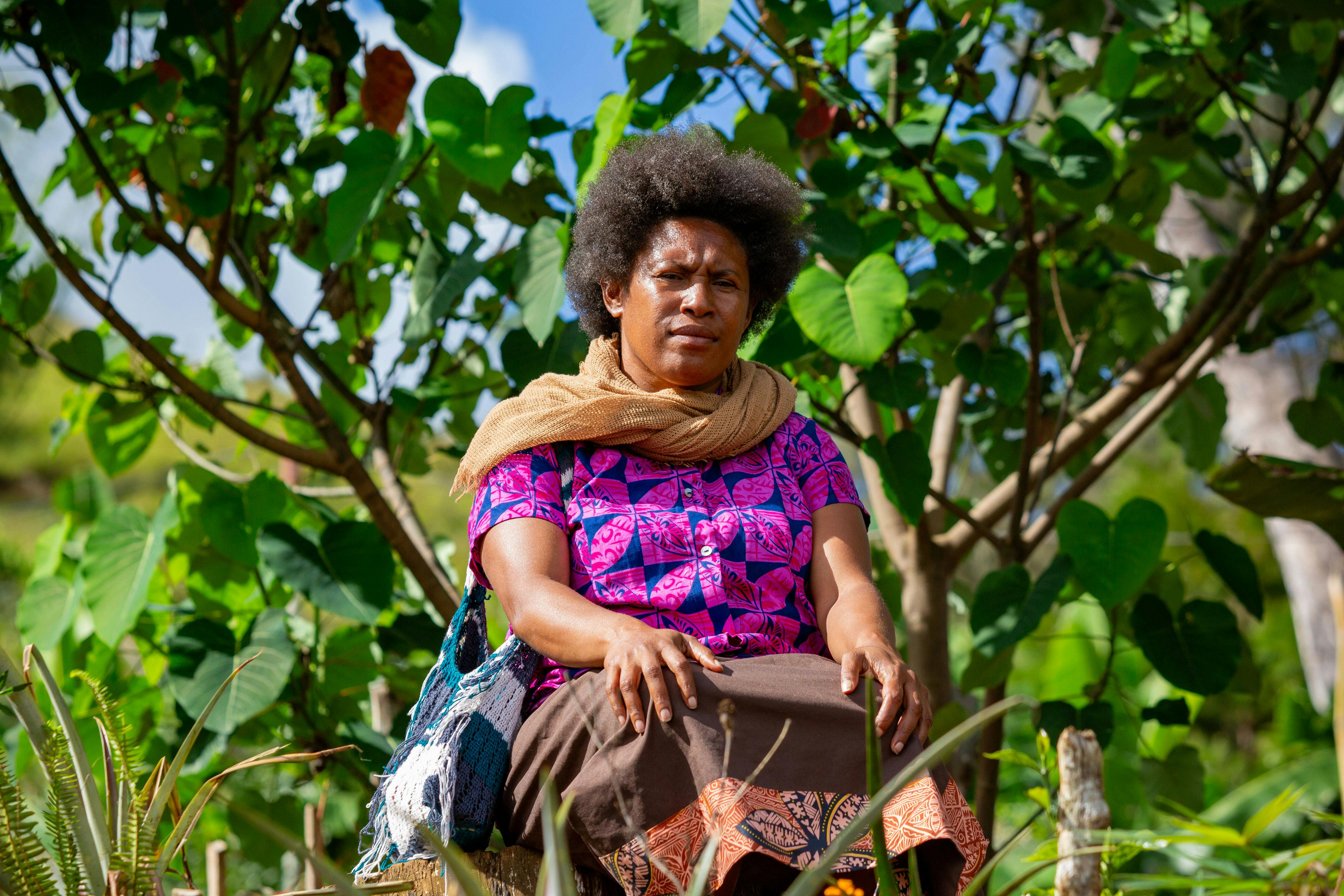 A woman sits among lush green foliage in Papua New Guinea, showcasing cultural attire.