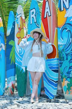 Smiling woman in summer attire posing by vibrant surfboards on a sunny beach day.