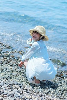 Smiling woman in straw hat captures a sunny day by the rocky beach.