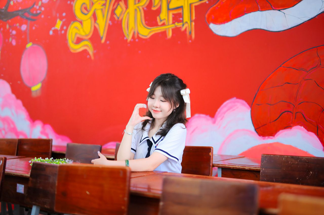 a student in uniform sits in a classroom with a vibrant red wall mural