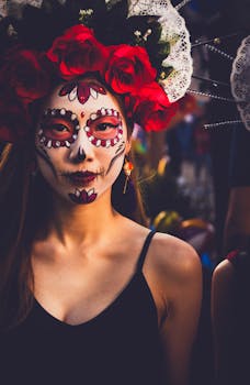 Vibrant portrait of a woman in traditional skull face paint and floral headpiece for Día de los Muertos.