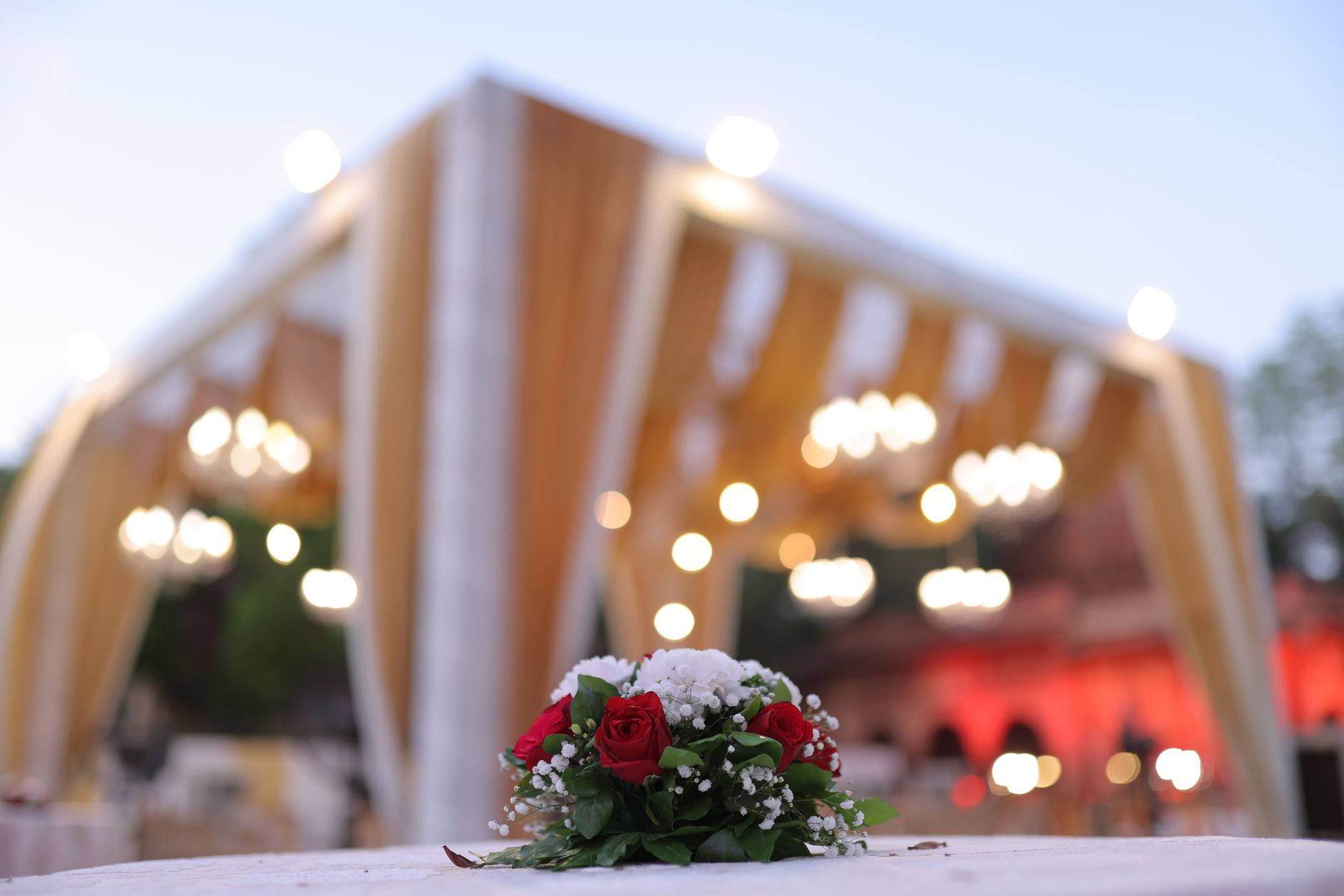 Beautiful outdoor wedding venue with red rose centerpiece and chandeliers.