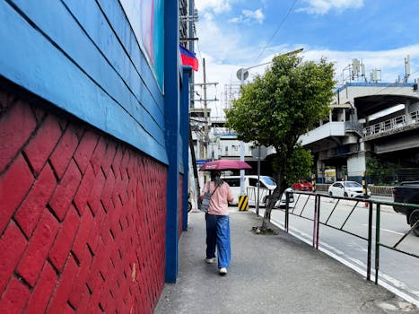 A woman walks along a colorful street in Quezon City, carrying an umbrella under a clear sky.