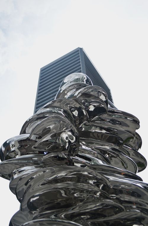Free Abstract metal sculpture with urban skyscraper backdrop under clear sky. Stock Photo