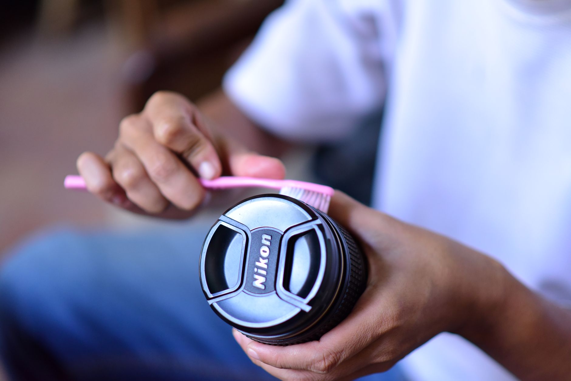 Someone cleaning a camera lens using a pink toothbrush, focusing on lens maintenance.