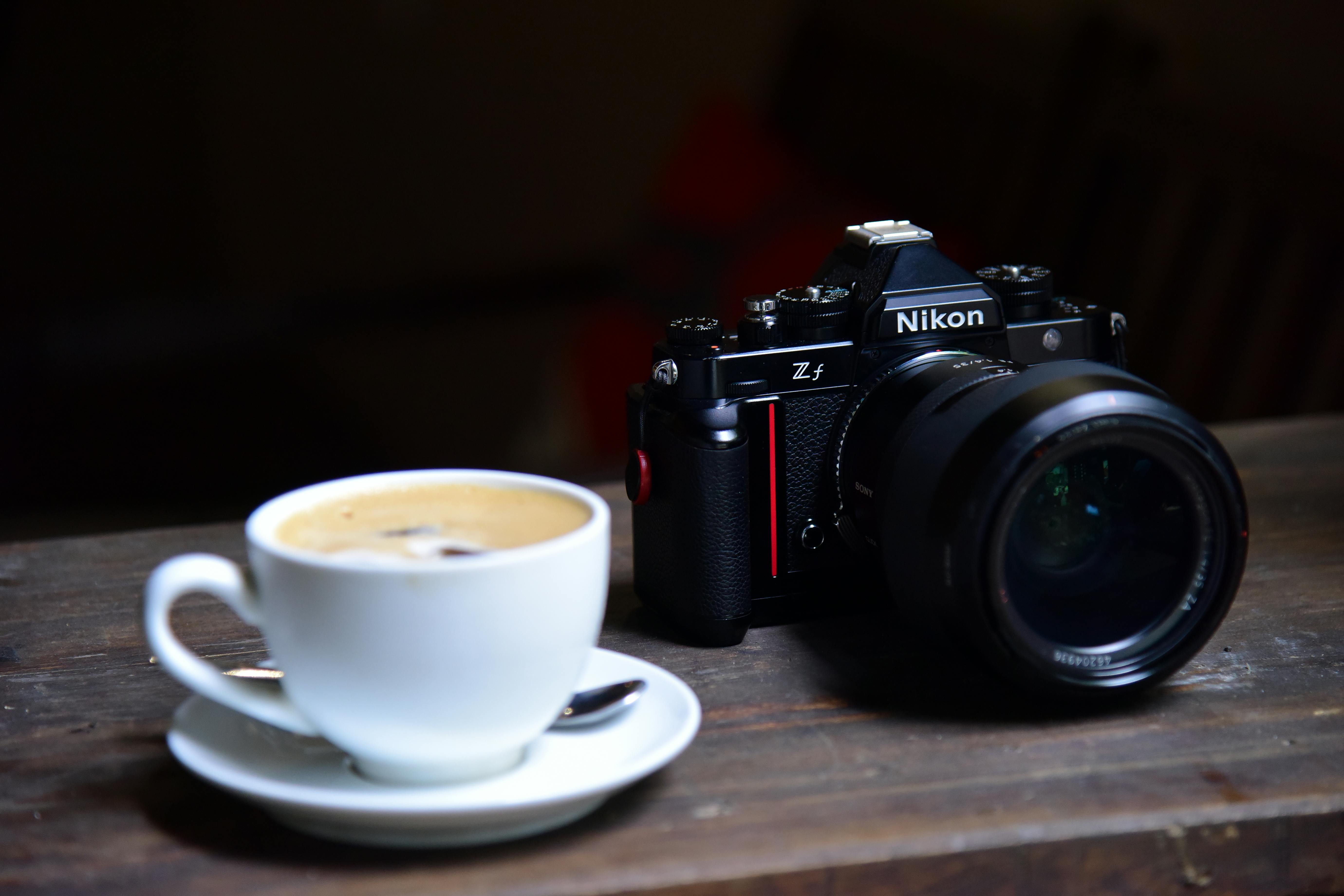 A Nikon camera with a coffee cup on a wooden table, reflecting a cozy setting.