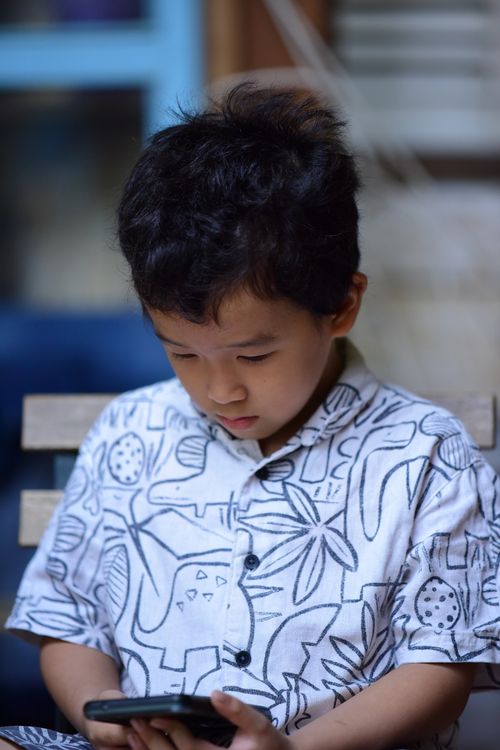 Free Young child deeply focused on smartphone while indoors, wearing patterned shirt. Stock Photo