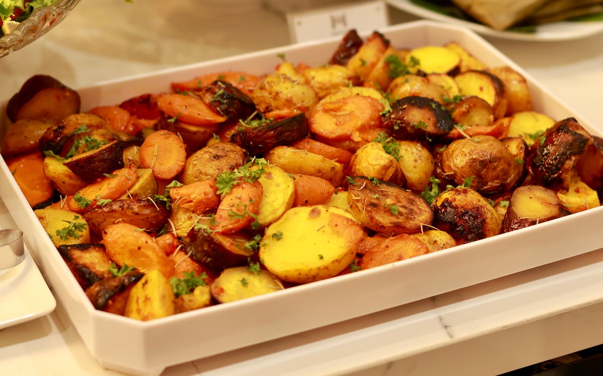 Colorful roasted potatoes and carrots garnished with herbs in a baking tray.