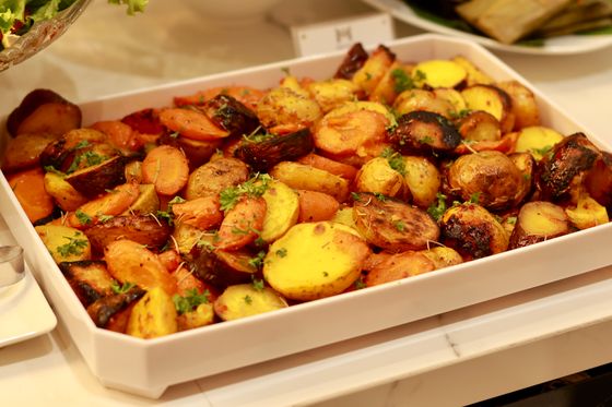 White rectangular dish of roasted sliced carrots and golden potatoes with chopped parsley