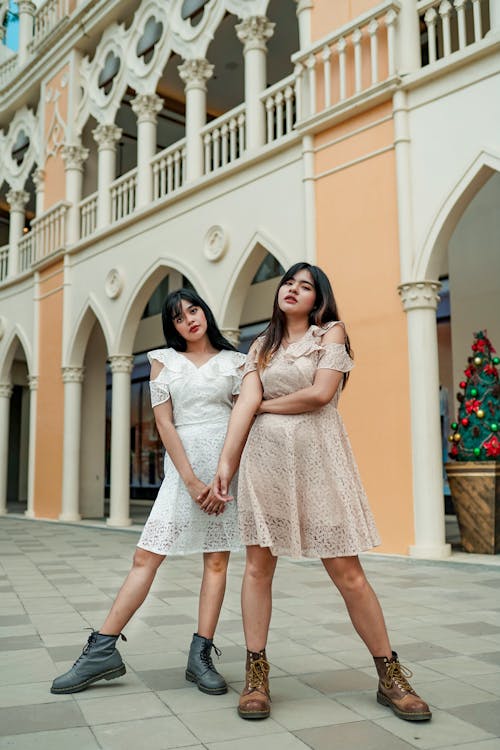 Two Women Wearing White and Brown Dresses Standing Beside Wall