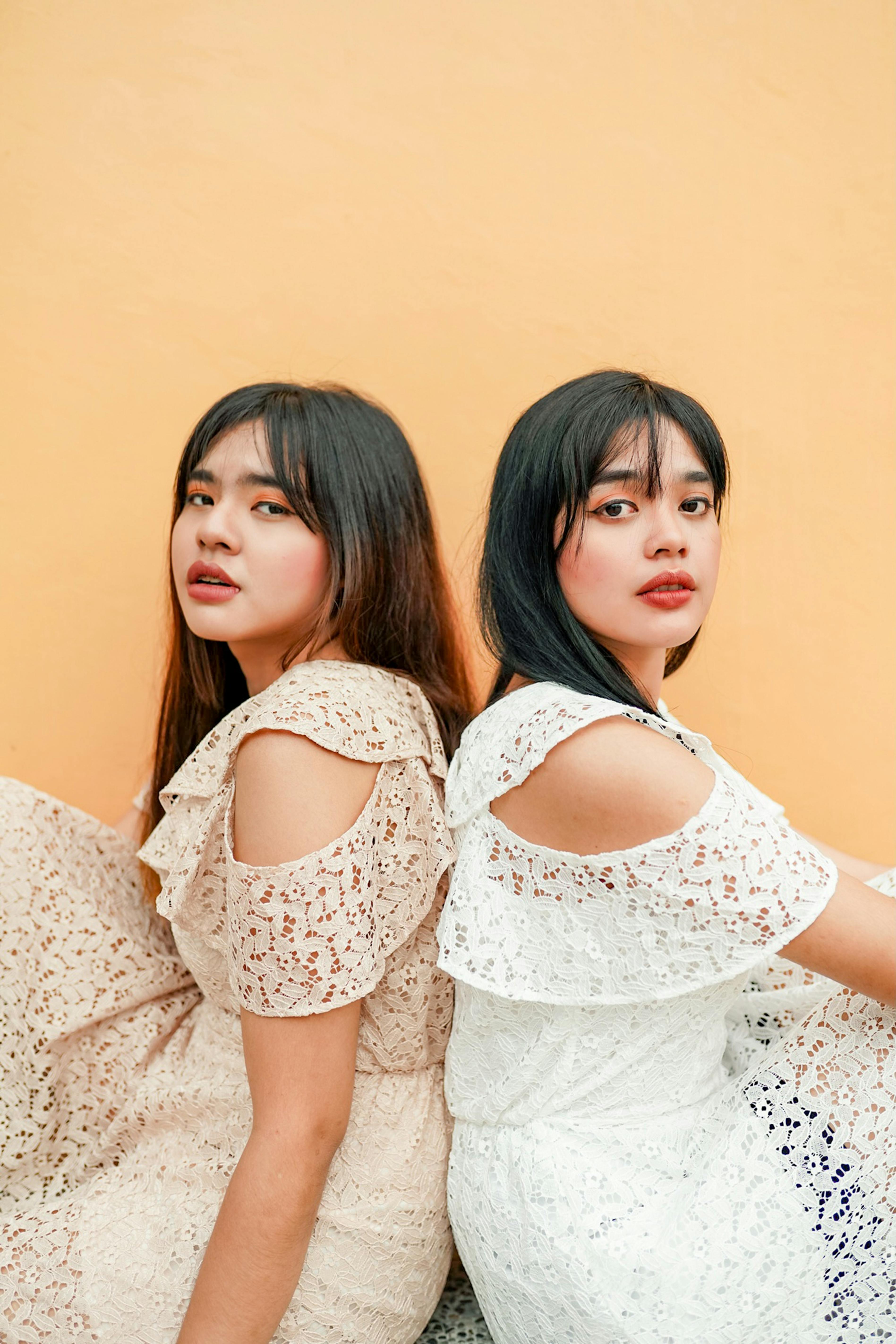 two woman sitting back to back wearing dress