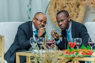 Two elegantly dressed men in suits enjoying a drink with straws at a social event.