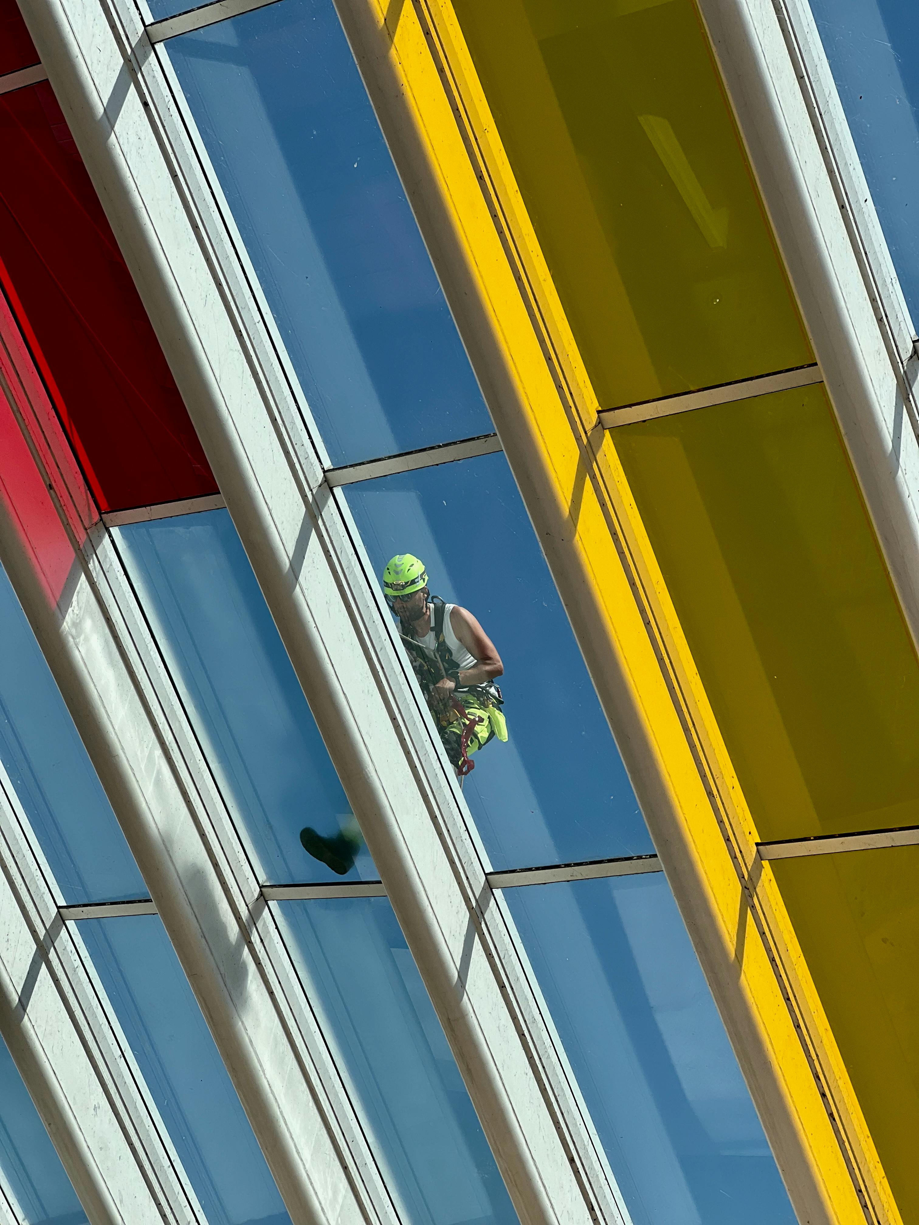 Gratuit Vedere din unghi mare a unui muncitor care curăță un acoperiș din sticlă vibrantă, cu panouri roșii, albastre și galbene. Fotografie de stoc