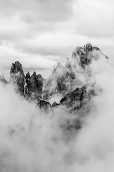 A dramatic black and white photograph showcasing the foggy peaks of the Dolomite Mountains in Italy.