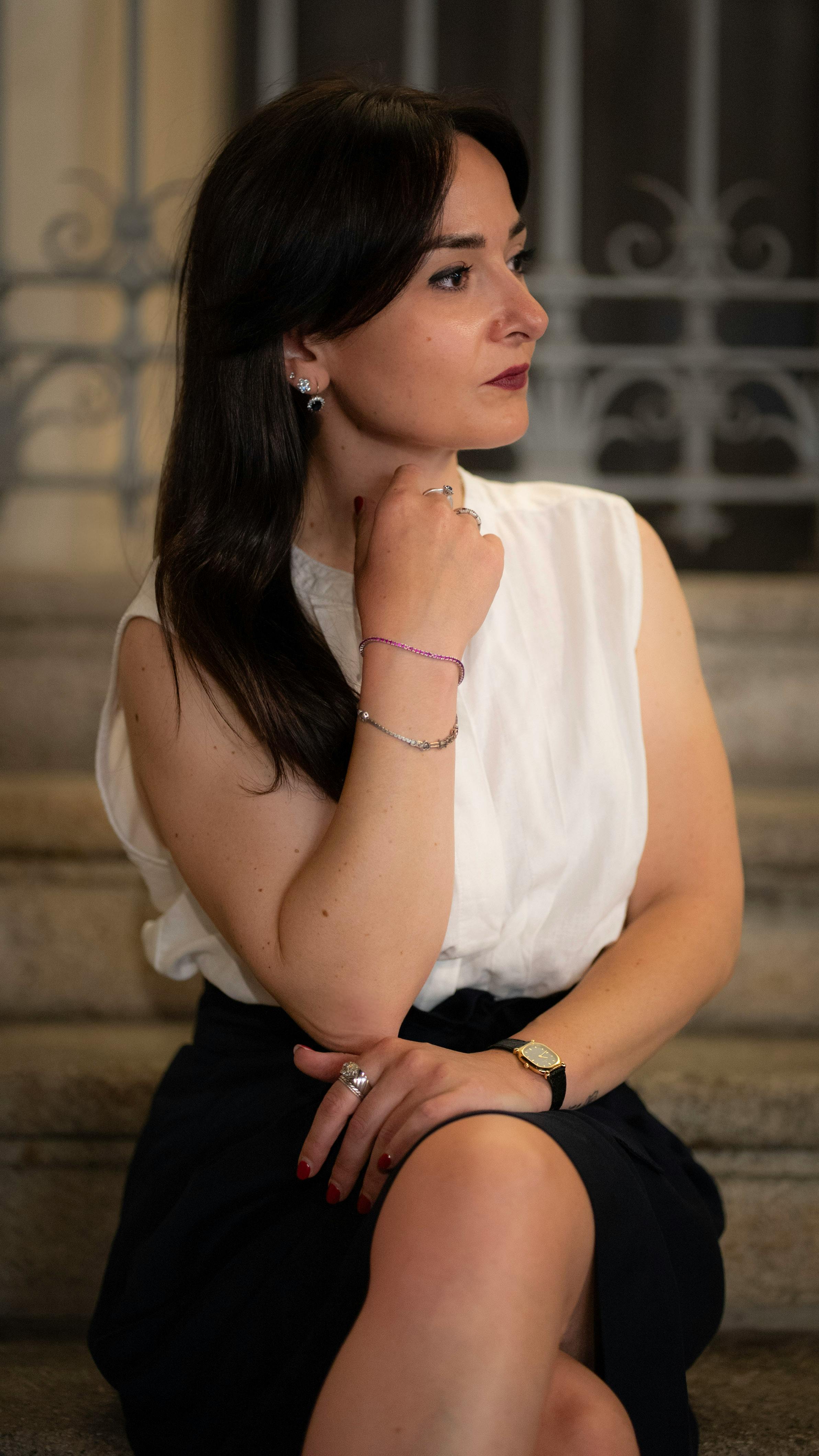 Stylish woman in white blouse and black skirt elegantly poses on steps in Milan, Italy.