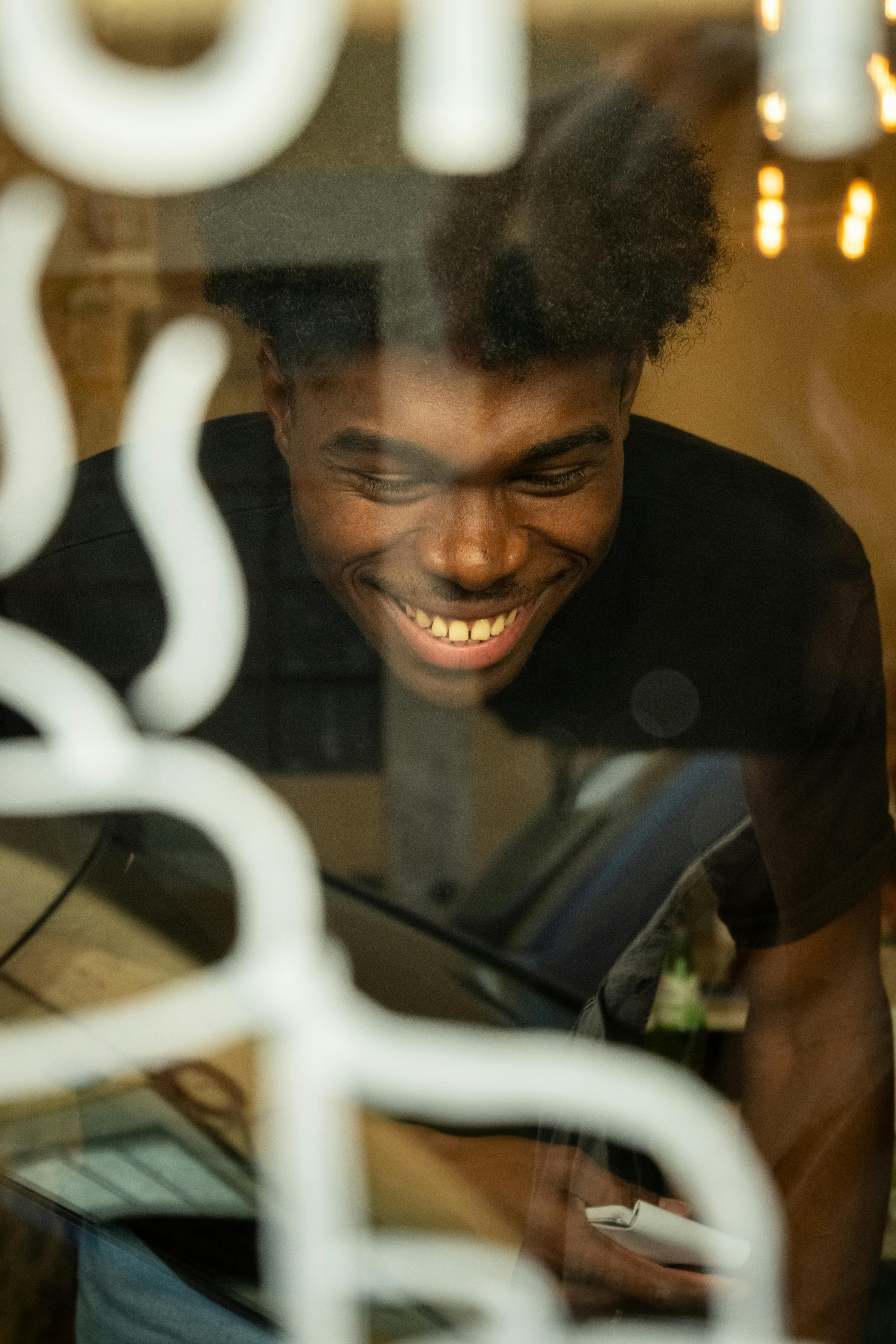 De franc Un jove alegre vist a través de l'aparador d'una cafeteria, irradiant felicitat i calidesa. Foto d'estoc