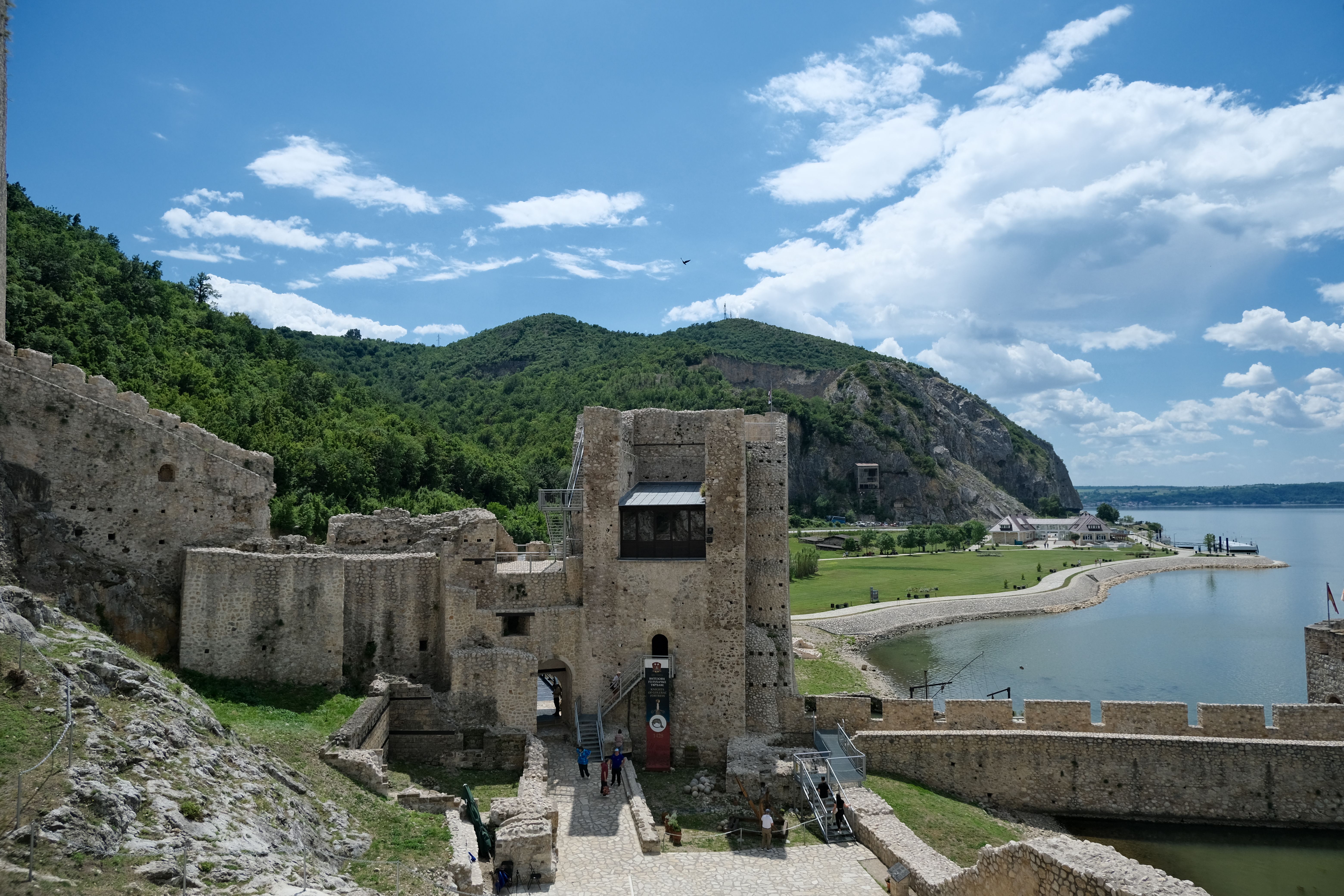 Scenic view of Golubac Fortress by the Danube River with lush greenery and blue sky.