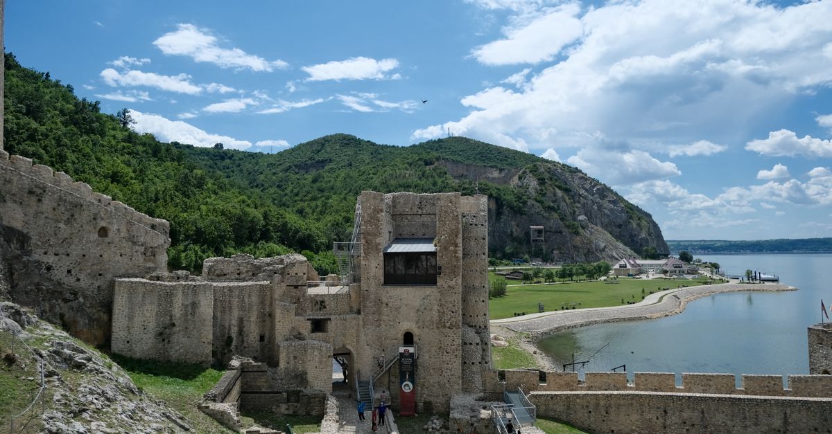 Scenic view of Golubac Fortress by the Danube River with lush greenery and blue sky.