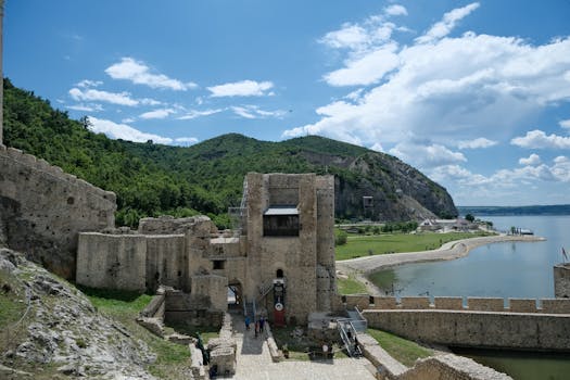 Scenic view of Golubac Fortress by the Danube River with lush greenery and blue sky.