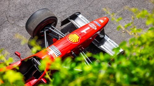 Free Aerial shot of a red Formula 1 car on a racetrack, surrounded by greenery. Stock Photo