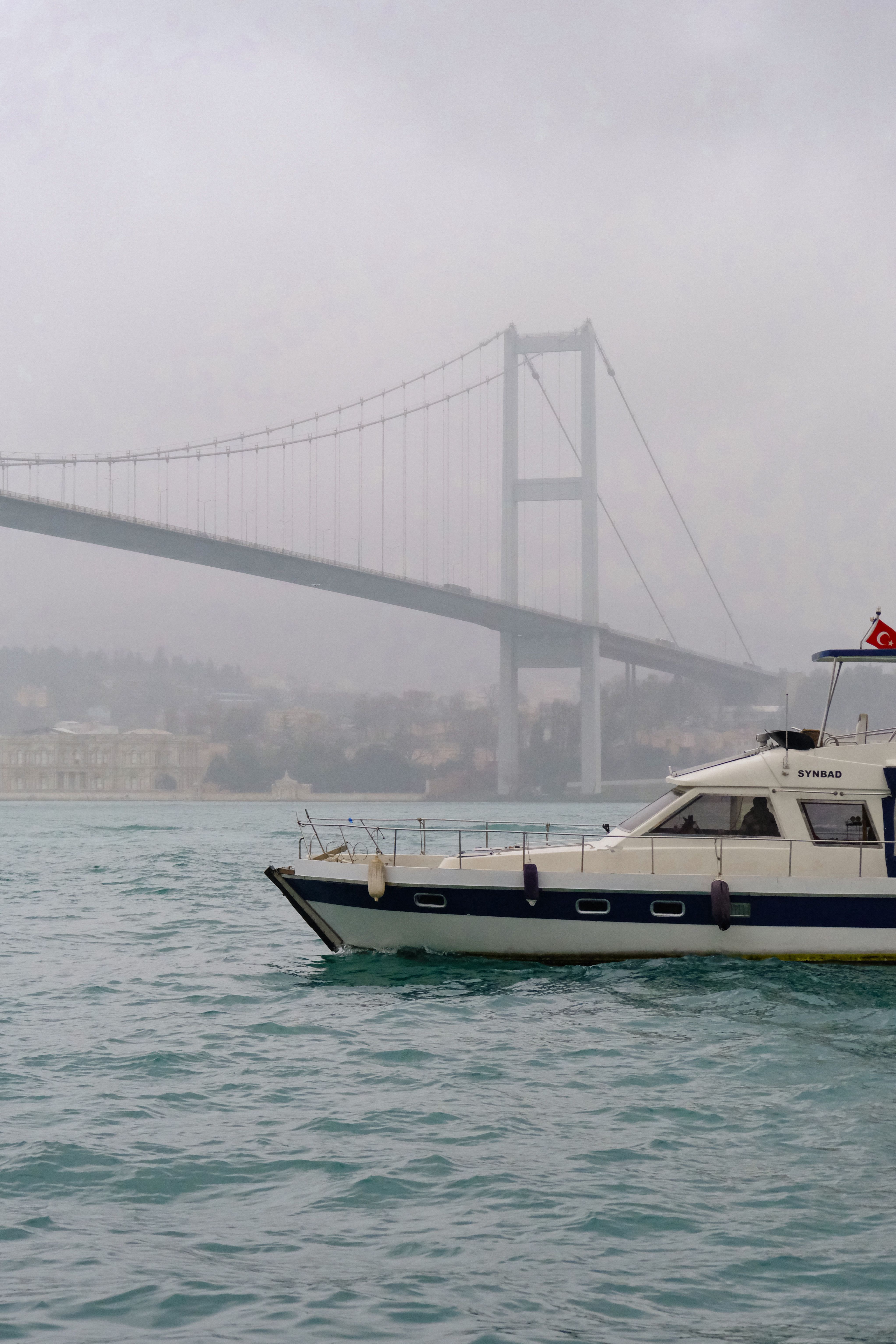 Free Boat sails on Bosphorus as fog envelops the bridge in Istanbul. Stock Photo