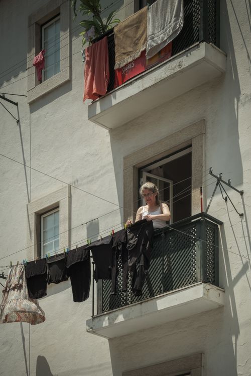 Free A woman hangs clothes on a balcony in Lisbon, capturing everyday life and architecture. Stock Photo
