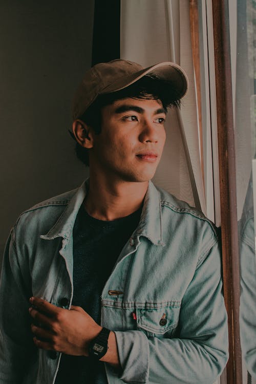 Man Wearing Cap and Denim Jacket Looking Out the Window