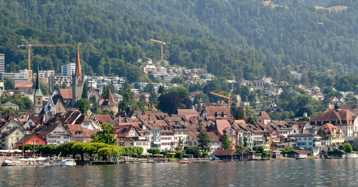 Malerische Ansicht von Zug mit Seeufer und gruenen Huegeln unter blauem Himmel