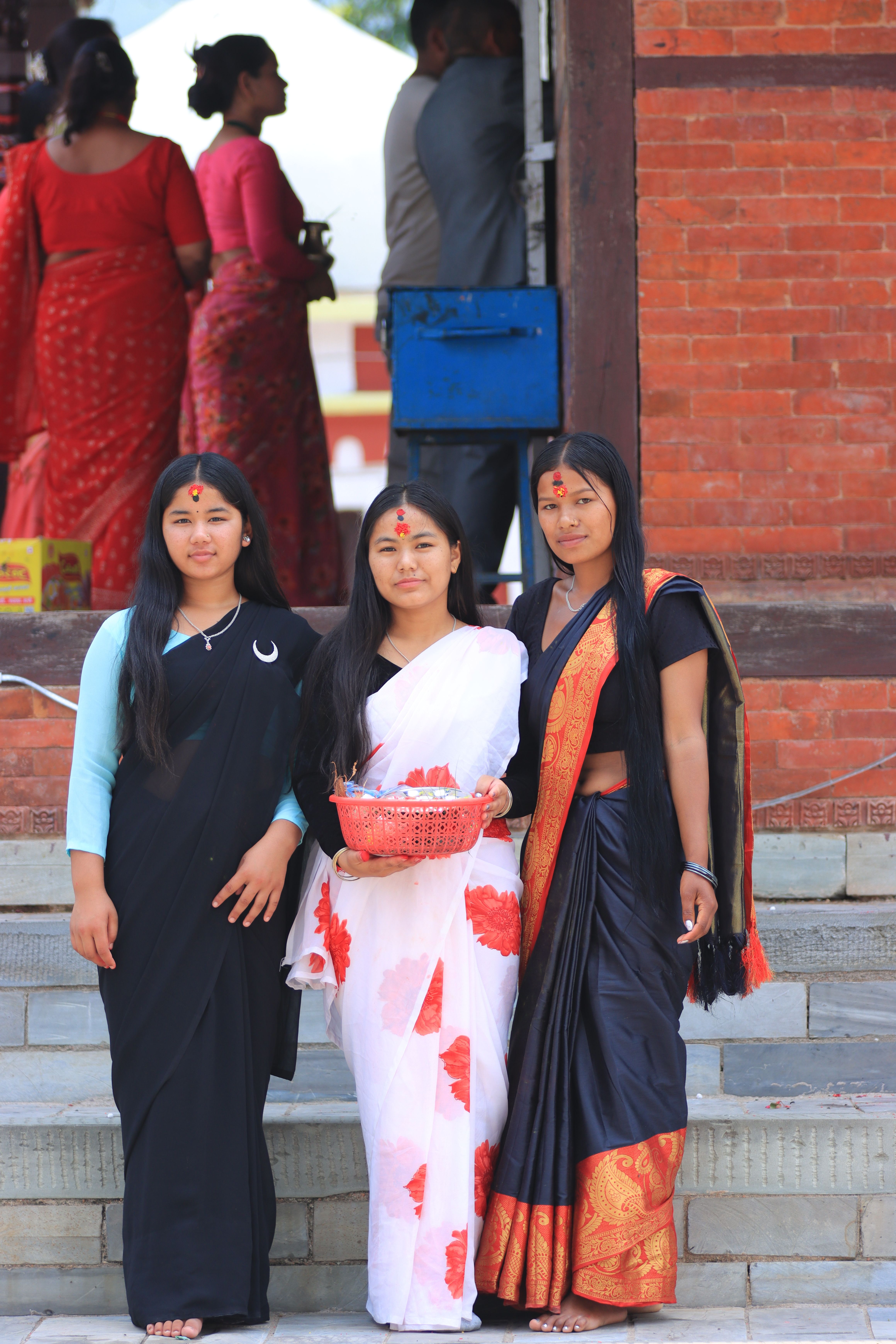 Three women in vibrant traditional dresses pose at a cultural event, showcasing rich cultural heritage.
