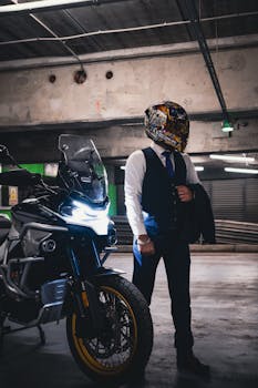Man in a suit with a futuristic helmet standing next to a motorcycle in a dim garage.