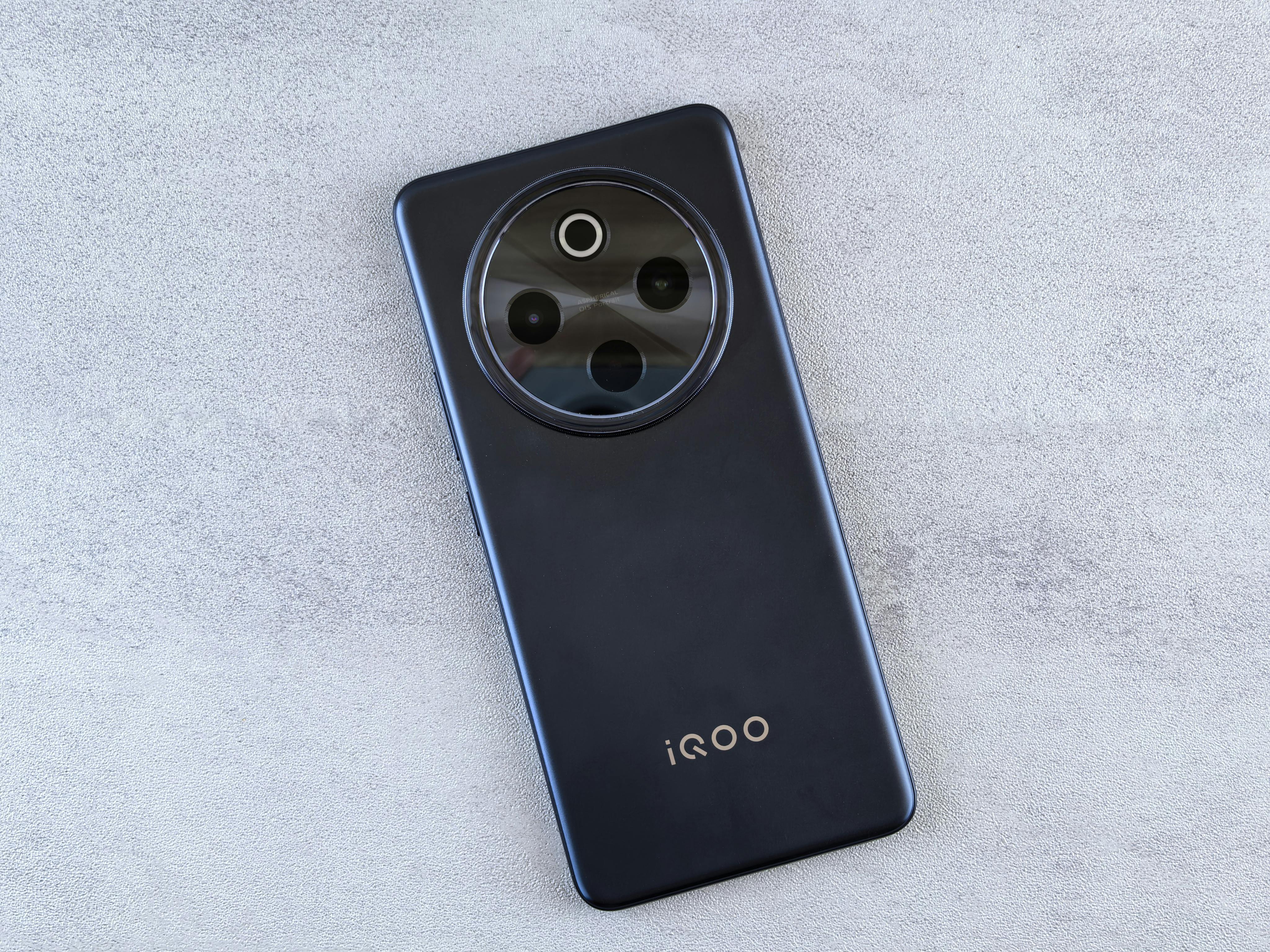 Top view of a modern iQOO smartphone on a textured concrete surface, showcasing design and camera arrangement.