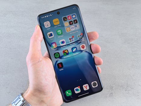 Close-up of a hand holding a smartphone displaying various app icons, showcasing modern technology and mobile interface.