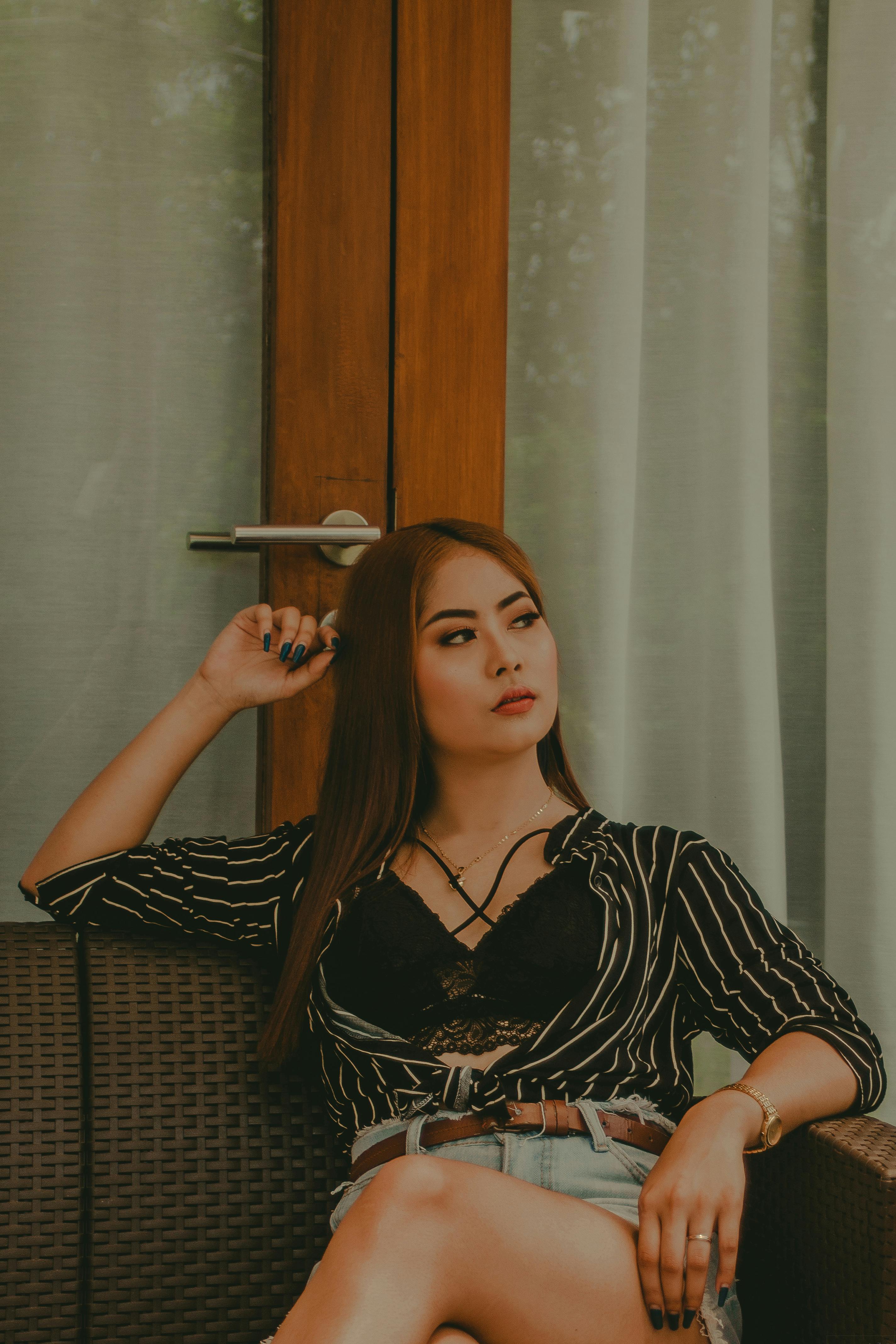 一位亚洲女子身着时尚服装，坐在室内的椅子上，散发着优雅与风格