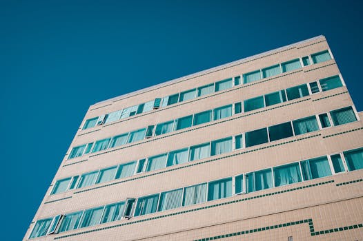 在晴朗的天空下，现代多层建筑的低视角、几何图案和蓝色窗户显得格外醒目